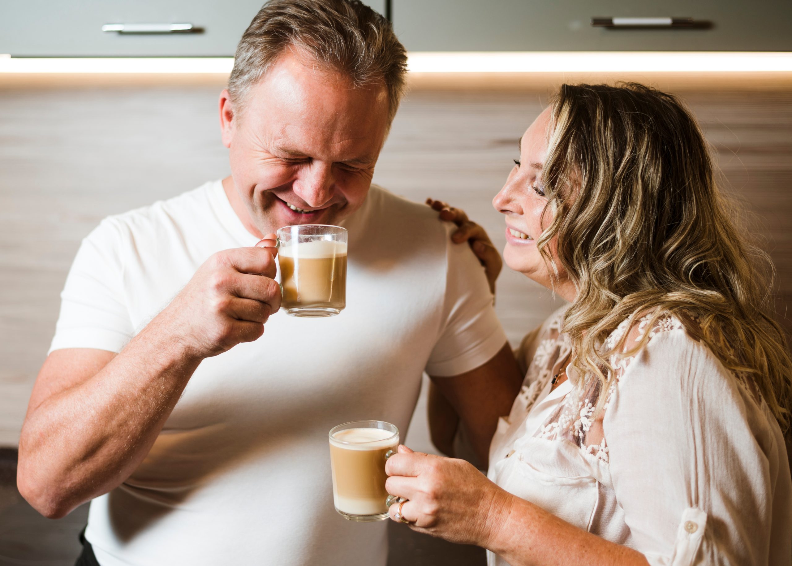 A couple laughing together holding coffee cups in a kitchen of a modern home