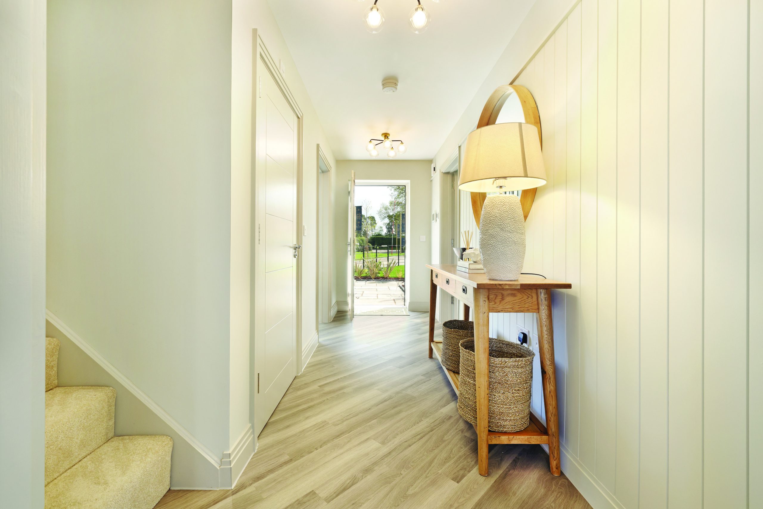 Well lit hallway with wooden floors, a console table with a lamp, and an open door leading to the front of the house