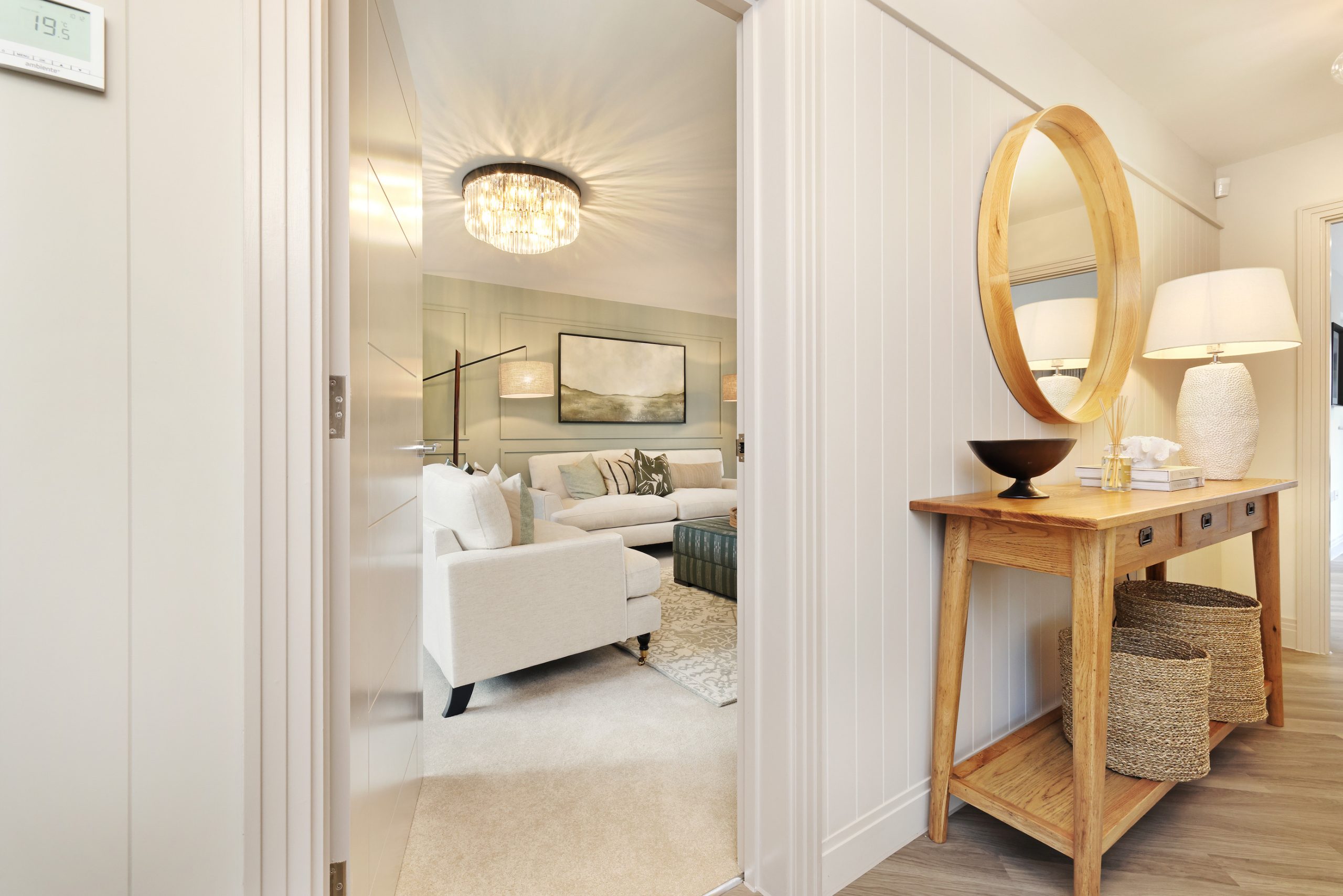 Living area viewed from hallway with a white and beige décor, and a mirror above a console table in the hallway.