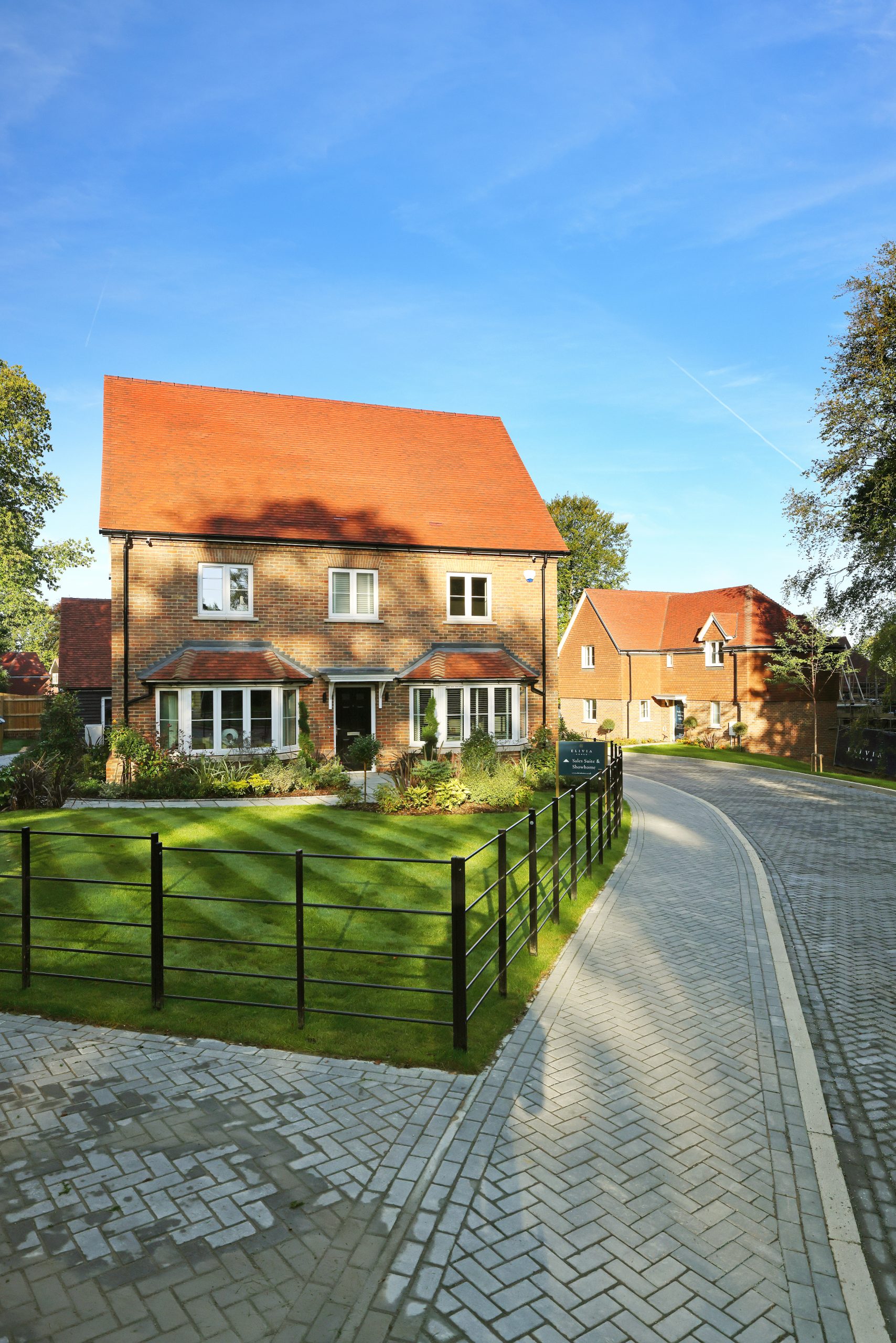 A modern brick home in a new housing development in the sunlight, with the shadow of a tree covering the front of it