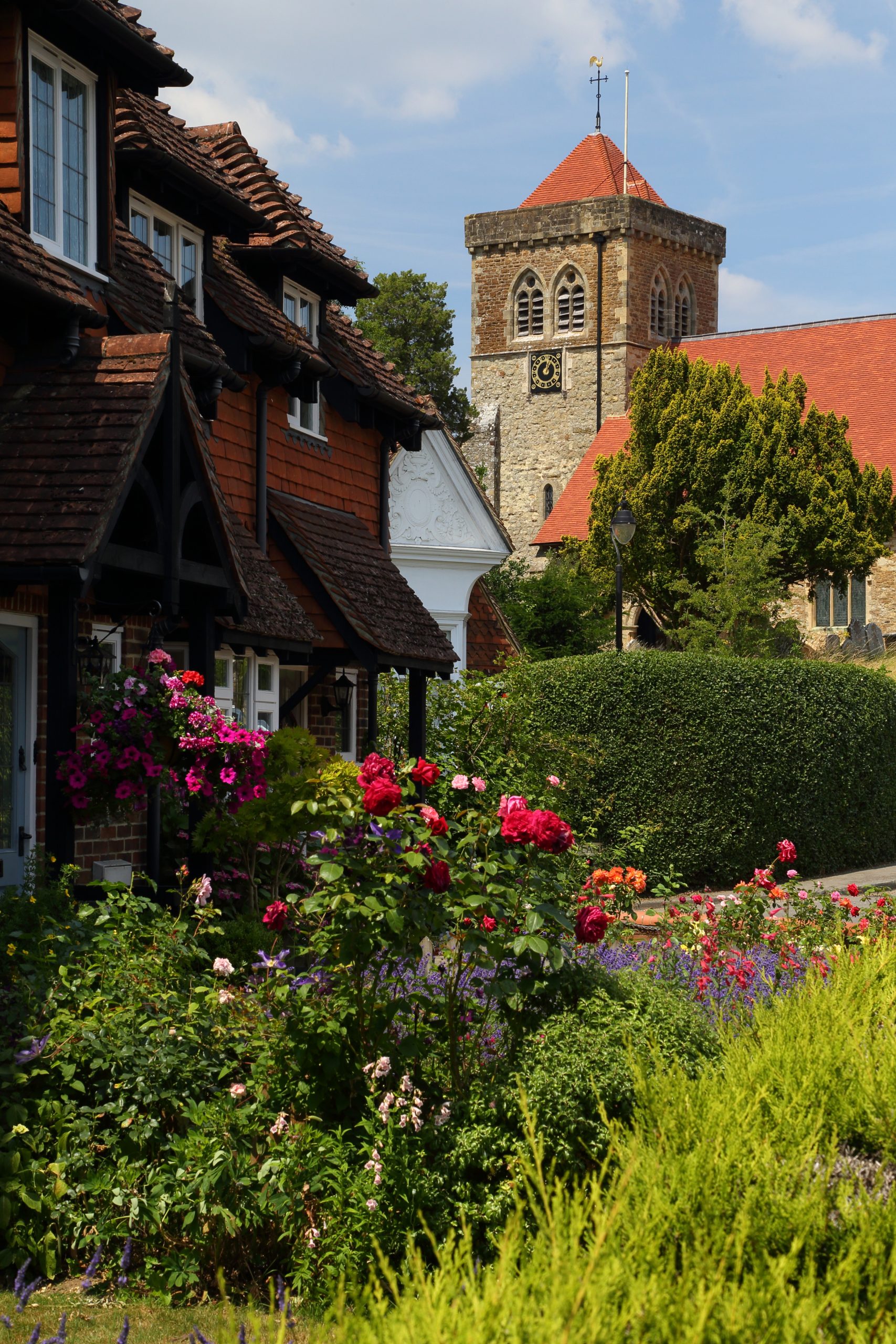 An old church building with a large clock on it surrounded by gardens and trees